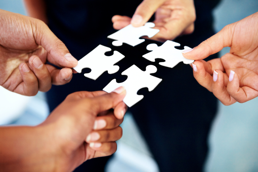 Closeup of a diverse group of people holding up pieces of a jigsaw puzzle