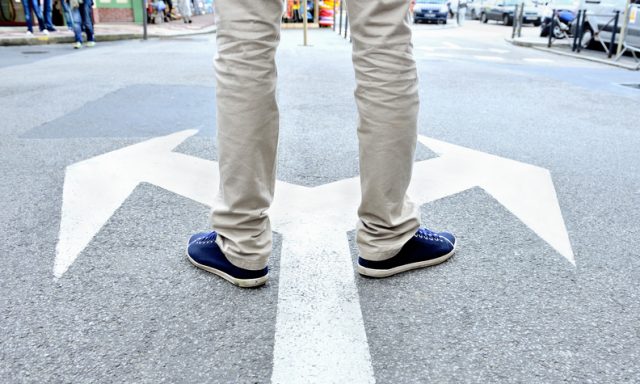 Arrows painted on asphalt. Young man standing hesitating to make a decision.