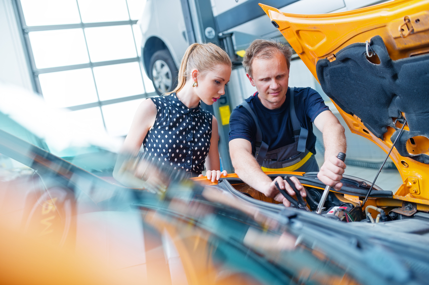 Auto mechanic with female customer looking under car hood.
