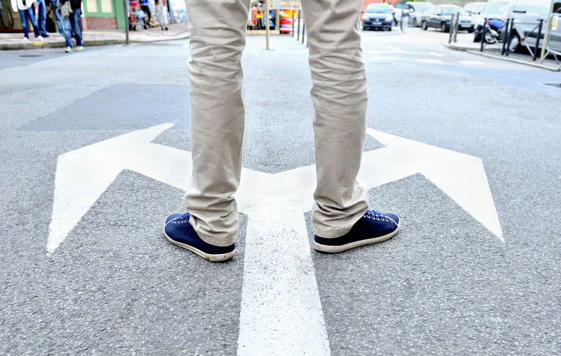 Arrows painted on asphalt. Young man standing hesitating to make a decision.